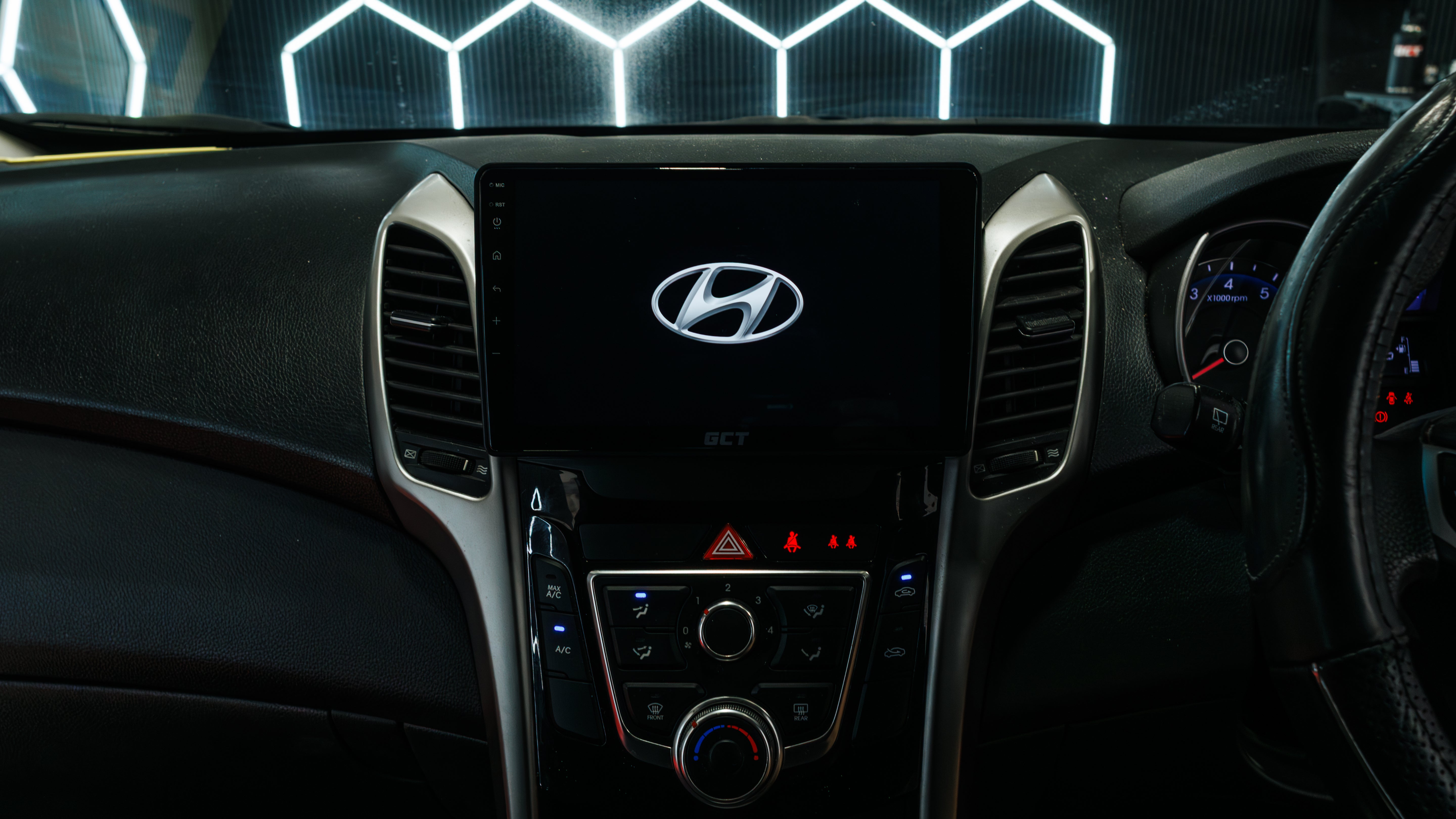 Close-up of a 2015 A 2015 Hyundai i30 dashboard with a large central touchscreen displaying the Hyundai logo, flanked by air vents and control buttons, with part of the steering wheel visible on the right.